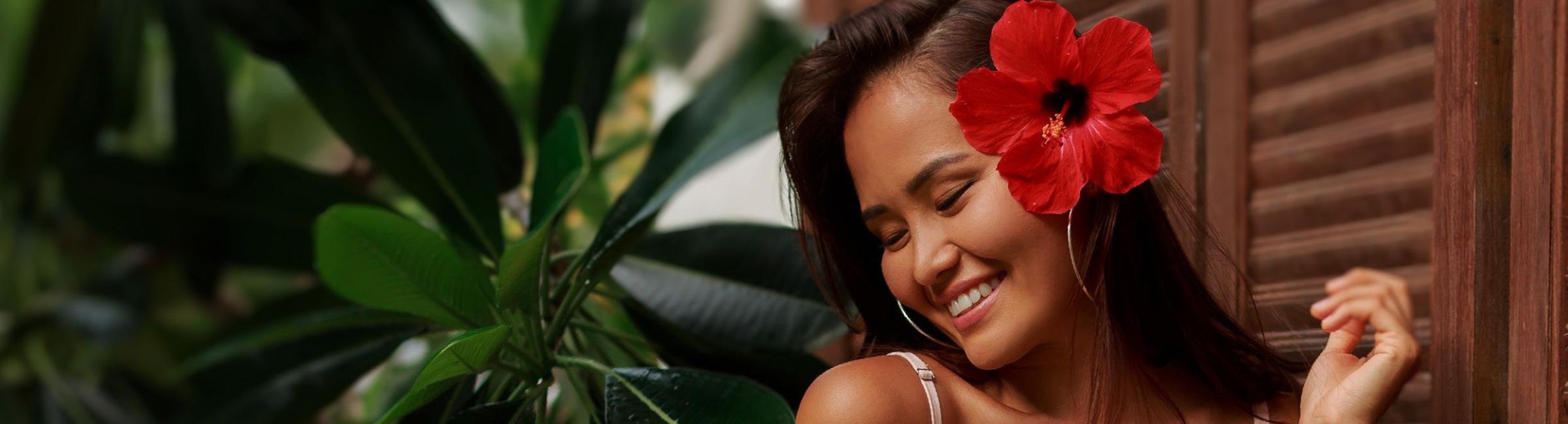 Lächelnde Frau mit einer roten Hibiskusblüte, Symbol für natürliche Schönheit und Tahitian-Noni-Energie